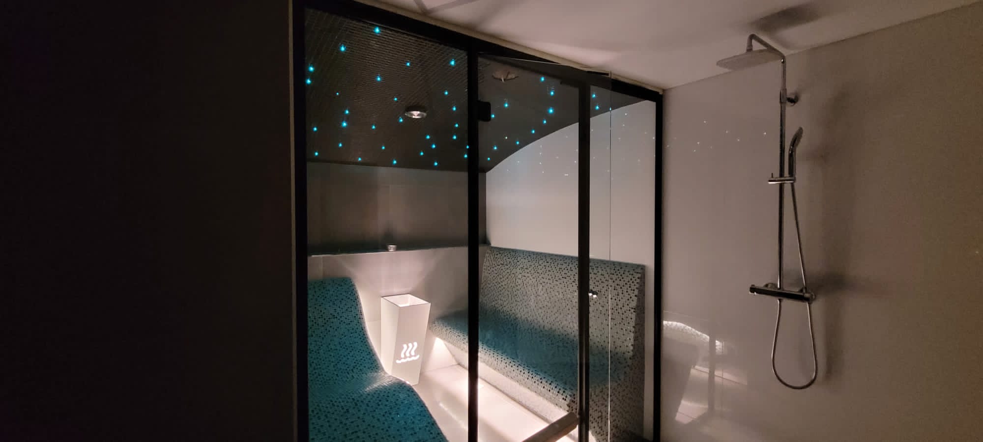 Steam room with teal mosaic loungers and starry ceiling